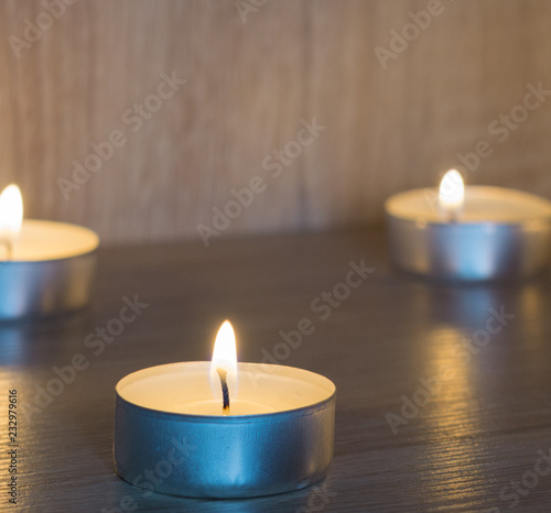 Close up of the flame of a burning round candle, on the back of a blurry background two lit candles.