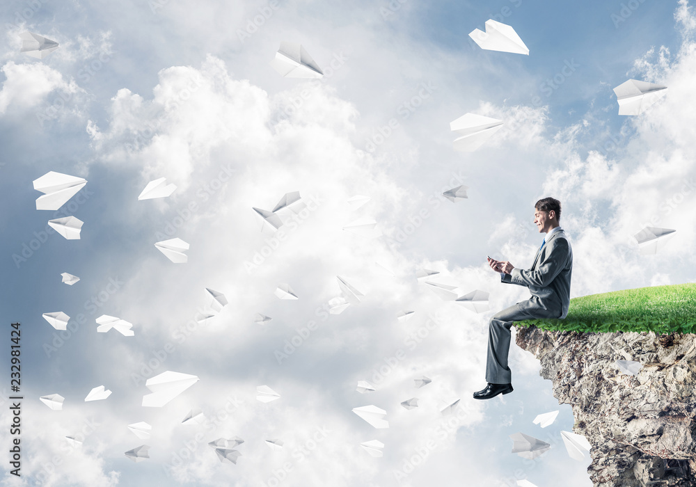 Elegant businessman on rock edge making calls and paper planes f Elegant businessman on rock edge making calls and paper planes f