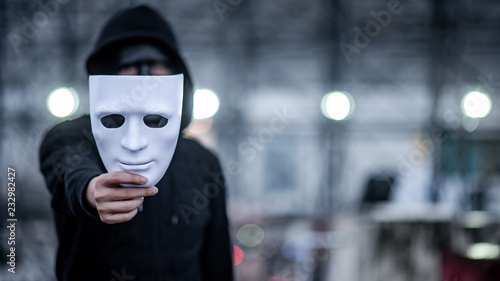 Bild auf Leinwand Mystery hoodie man with black mask holding white mask in his hand