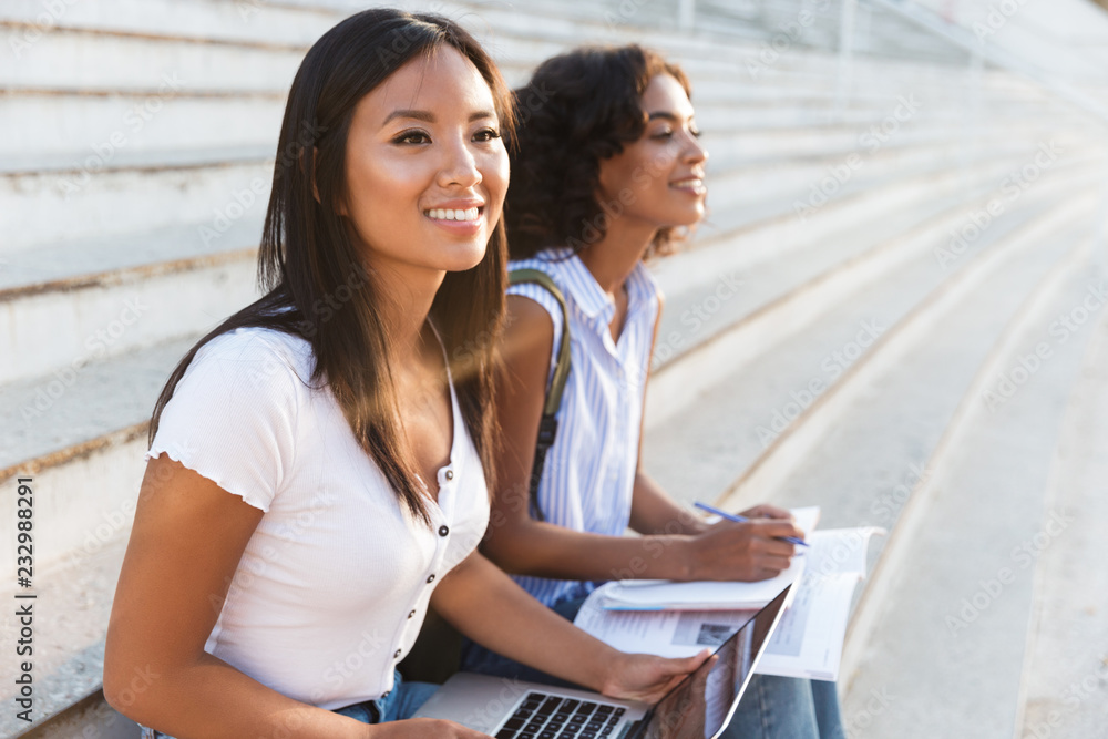 Fototapeta premium Two happy young multhiethic students girls studying