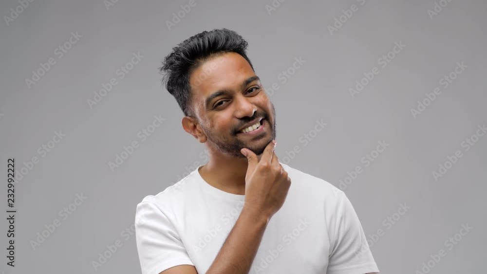 grooming and people concept - smiling indian man touching his beard over gray background grooming and people concept - smiling indian man touching his beard over gray background