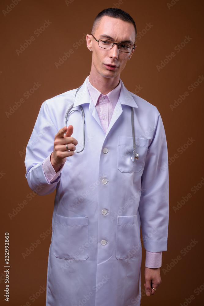 Young handsome androgynous man doctor against brown background Young handsome androgynous man doctor against brown background