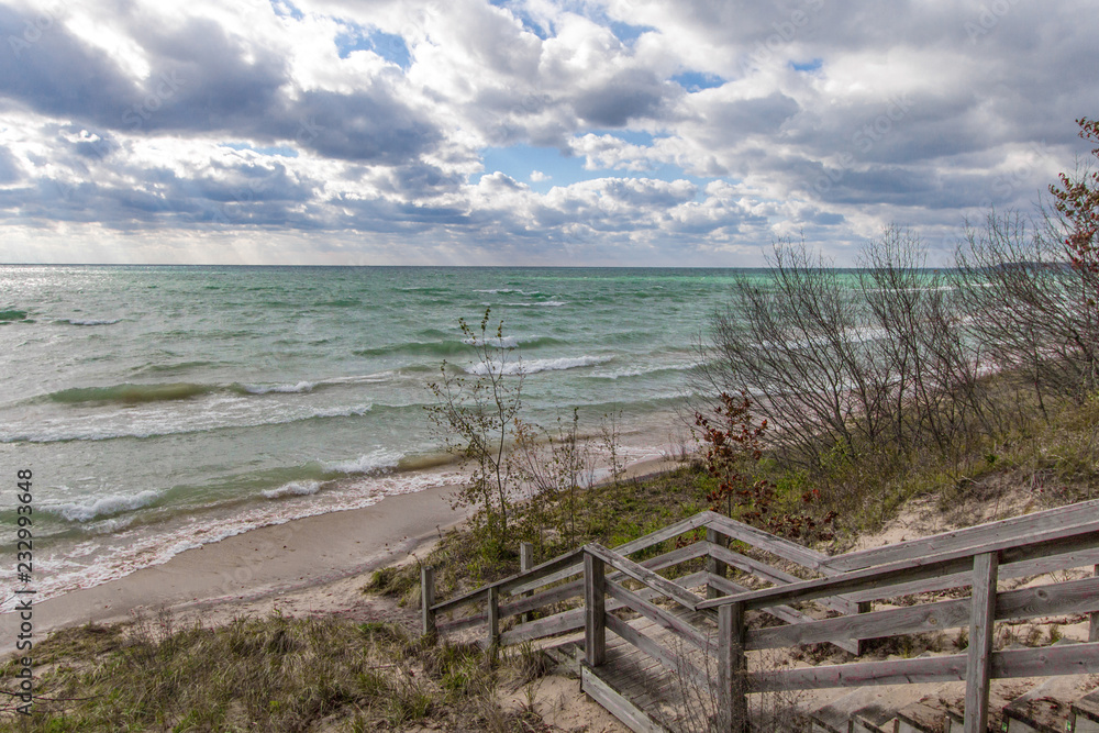 Stairs To The Beach. Wooden staircase leads to a wide sandy beach on the shore of scenic Lake Michigan on a beautiful and windy summer day. Stairs To The Beach. Wooden staircase leads to a wide sandy beach on the shore of scenic Lake Michigan on a beautiful and windy summer day.