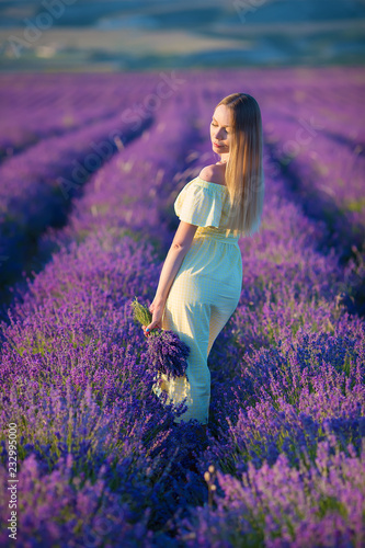 Fototapeta Naklejka Na Ścianę i Meble -  Smiling beautiful blond lady model on lavender field enjoy summer day wearing airy whit dress with bouquet of flowers.