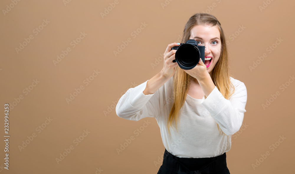 Obraz premium Young woman with a professional digital SLR camera on a brown background