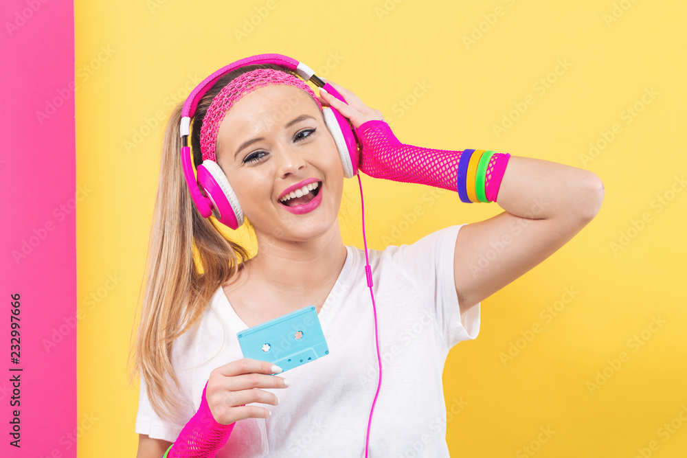Woman in 1980's fashion holding a cassette tape on a split yellow and pink background