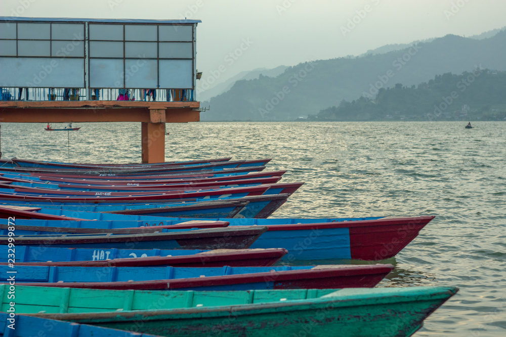 Red blue green wooden boats at the pier on the water in cloudy weather. lake on the background of the mountains.