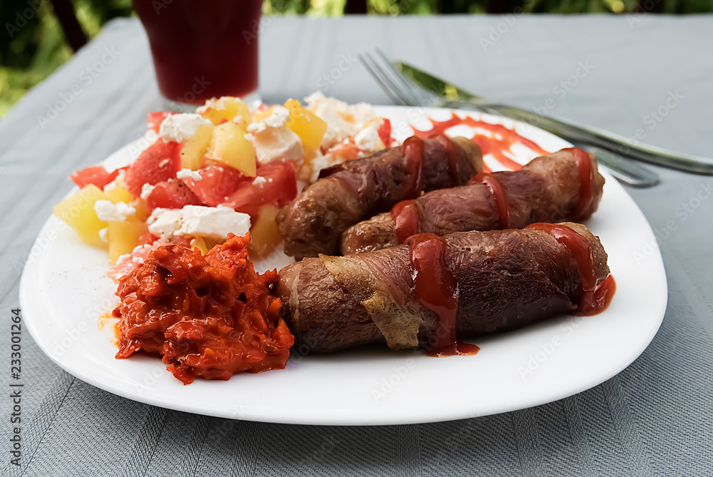 Chevapchichi. Meat sausages with vegetable salad, ketchup and adjika on white plate. Dish of Balkan cuisine. Chevapchichi. Meat sausages with vegetable salad, ketchup and adjika on white plate. Dish of Balkan cuisine.