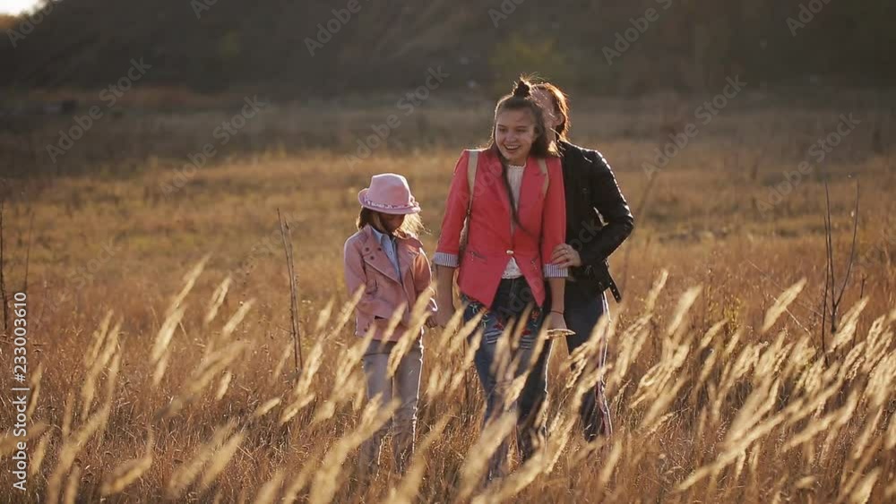 A happy mother and her two daughters are walking around the field in the steppe at sunset A happy mother and her two daughters are walking around the field in the steppe at sunset