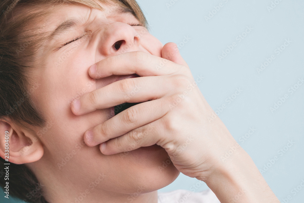 Boy yawns with his eyes closed, covering his mouth with his palm Boy yawns with his eyes closed, covering his mouth with his palm