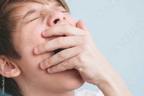 Boy yawns with his eyes closed  covering his mouth with his palm