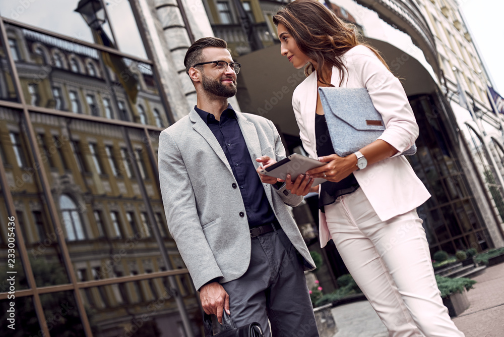 Using gadget. Two young business people standing outside on the city street using digital tablet checking latest news smiling joyful Using gadget. Two young business people standing outside on the city street using digital tablet checking latest news smiling joyful
