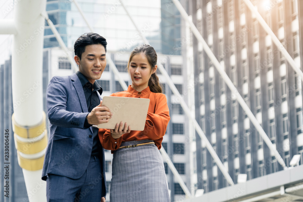 a couple of business man and business woman read content on tablet and stand with city background a couple of business man and business woman read content on tablet and stand with city background