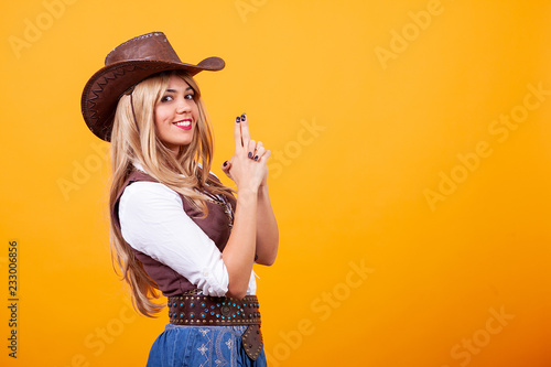 Print op canvas Beautiful young woman wearing cowboy costume over yellow background