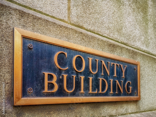 Exterior sign that reads "County Building" in brass letters. Graphic resource.