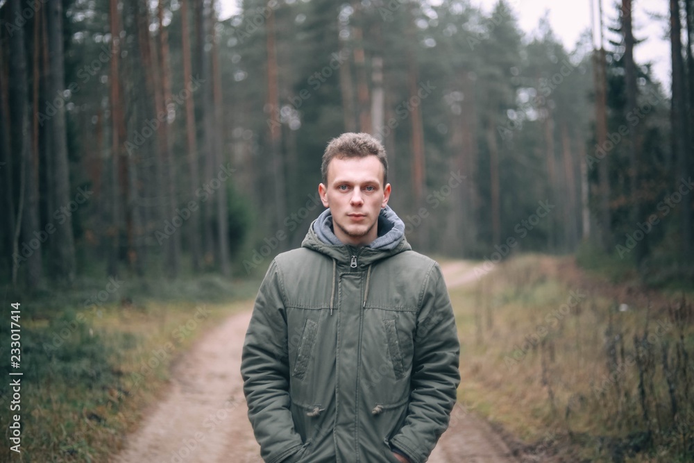  Caucasian young man in a forest in a green jacket.