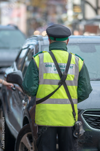 portrait of civil enforcement officer traffic warden about to hand out ticket when owner returns and places hand on car door on a rainy day photo