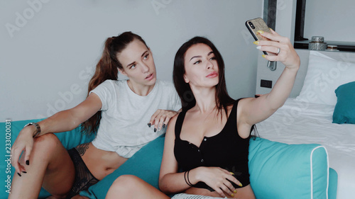 Happy women friends doing selfie photo while sitting on the sofa in modern interior house. Free time, weekend with friends concept