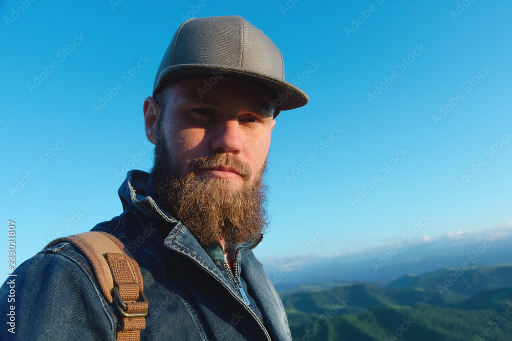 Portrait of a bearded stylish traveler in a cap against a blue sky. Time to travel concept