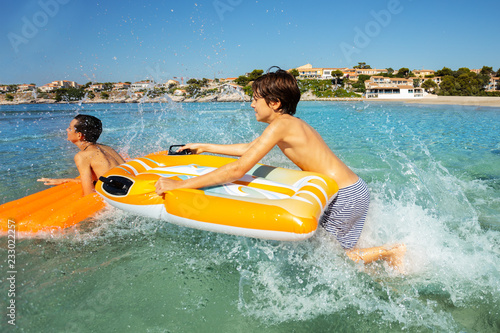 Happy boys riding the waves with air mattresses