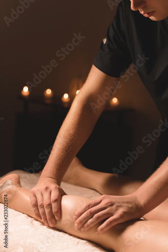 Canvastavla Close-up of male hands doing calf massage of female legs in a dark room with candles in the background