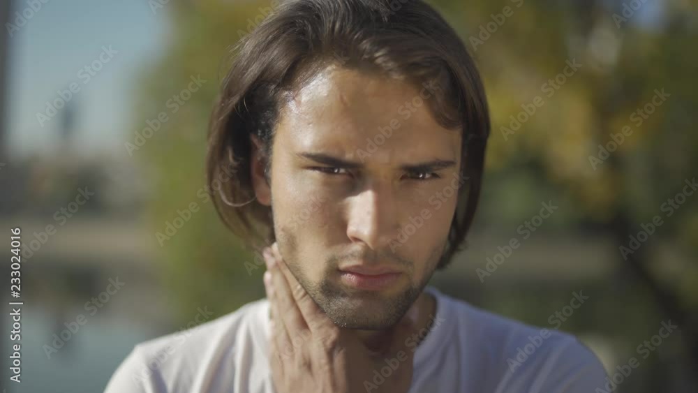 Handsome male looks at the camera standing in the park. Face of young man closeup Handsome male looks at the camera standing in the park. Face of young man closeup