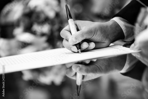 Foto b/n di una mano che firma di un contratto con riflesso su tavolo  photo