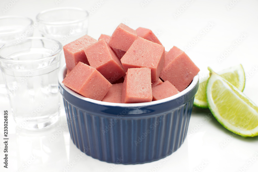 Traditional Brazilian cold cut cubes called mortadela in a white pub table with sugarcane liquor in the background Traditional Brazilian cold cut cubes called mortadela in a white pub table with sugarcane liquor in the background