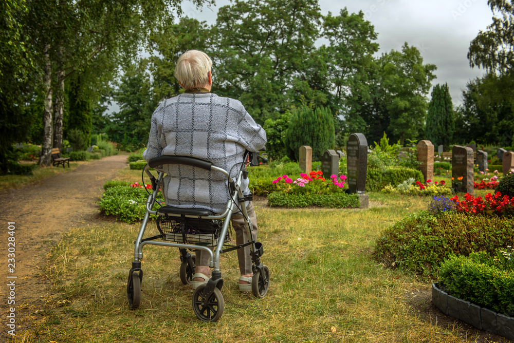 An old woman goes with her walking frame on the graveyard to be there with her survivors. Concept: mobility in old age or health An old woman goes with her walking frame on the graveyard to be there with her survivors. Concept: mobility in old age or health