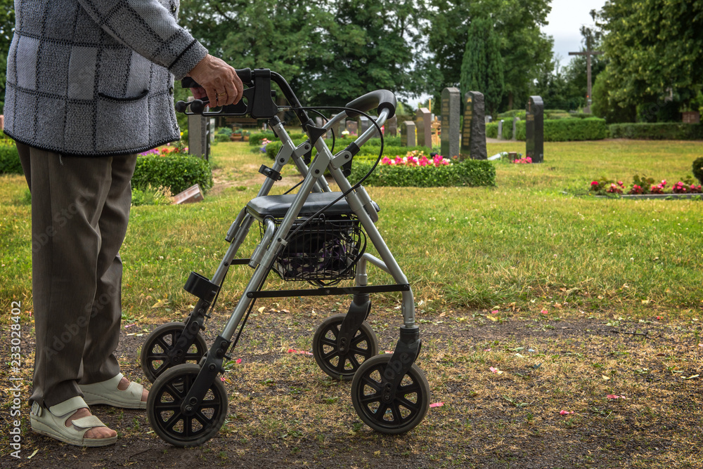 Obraz premium An old woman goes with her walking frame on the graveyard to be there with her survivors. Concept: mobility in old age or health