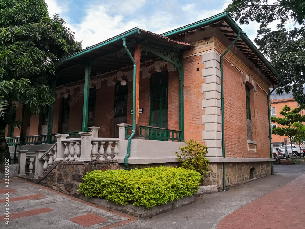 Traditional colonial house with Latin and Spanish architecture. Detail of the structure made of brown bricks and roof of clay tiles with green wood columns and large porch.