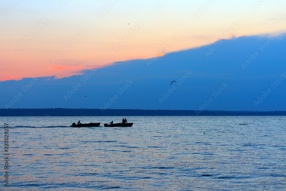 The silhouettes of two fishing boats with fishermen in the lake at dusk after sunset