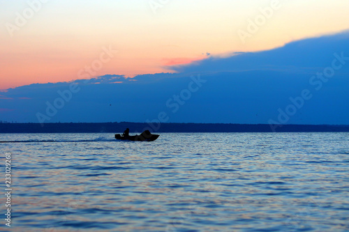 Silhouette of fishing boat with fisherman in the lake at dusk after sunset