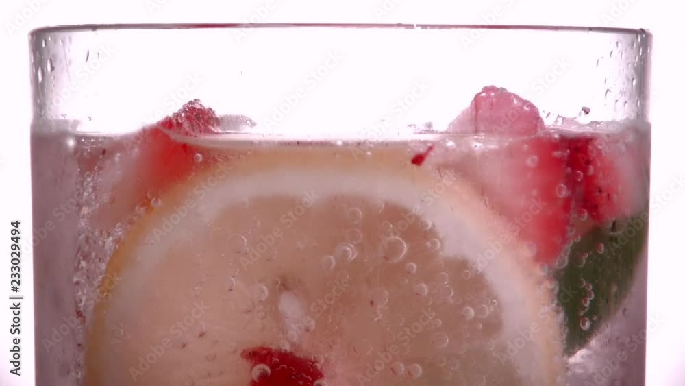 Close up of drinking glass with strawberries, lemon, lime and ice cubes floating in Sparkling water Close up of drinking glass with strawberries, lemon, lime and ice cubes floating in Sparkling water