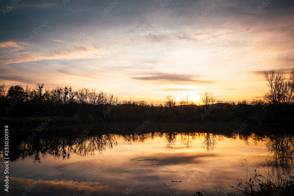 The lake during sunset looking at the water and the trees on the other side of the shadows.