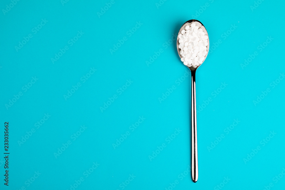 Sugar substitute pills in a spoon, on a blue background Sugar substitute pills in a spoon, on a blue background
