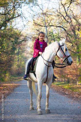 A girl rides a white horse in the forest