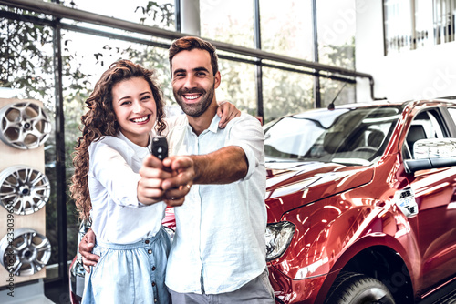 Portrait of a happy young couple hugging in a car salon showing car keys to a newly bought vehicle