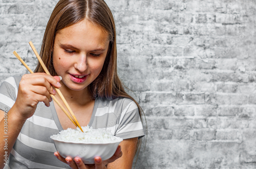 portrait of young teenager brunette girl with long hair eating rice on gray wall background portrait of young teenager brunette girl with long hair eating rice on gray wall background