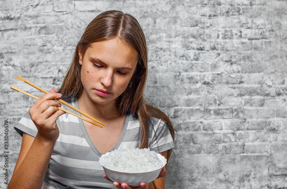 portrait of young teenager brunette girl with long hair eating rice on gray wall background portrait of young teenager brunette girl with long hair eating rice on gray wall background