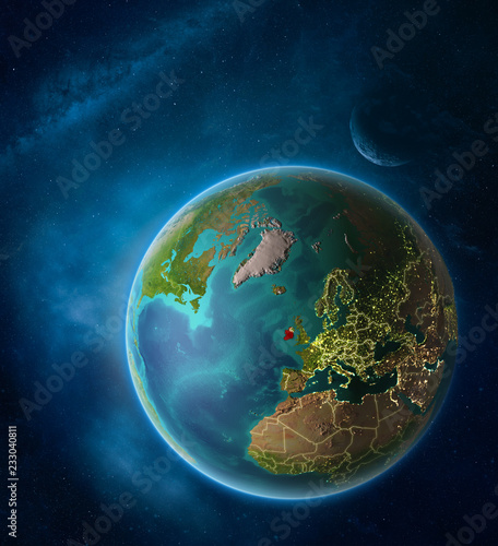 Planet Earth with highlighted Ireland in space with Moon and Milky Way. Visible city lights and country borders.