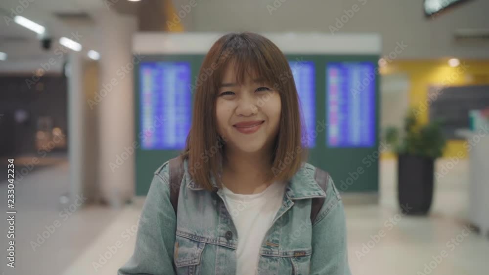 Slow motion - Happy Asian woman smiling to camera while staying at terminal in international airport, female tourist ready to travel on vacation. Lifestyle women happy holiday in the airport concept. Slow motion - Happy Asian woman smiling to camera while staying at terminal in international airport, female tourist ready to travel on vacation. Lifestyle women happy holiday in the airport concept.