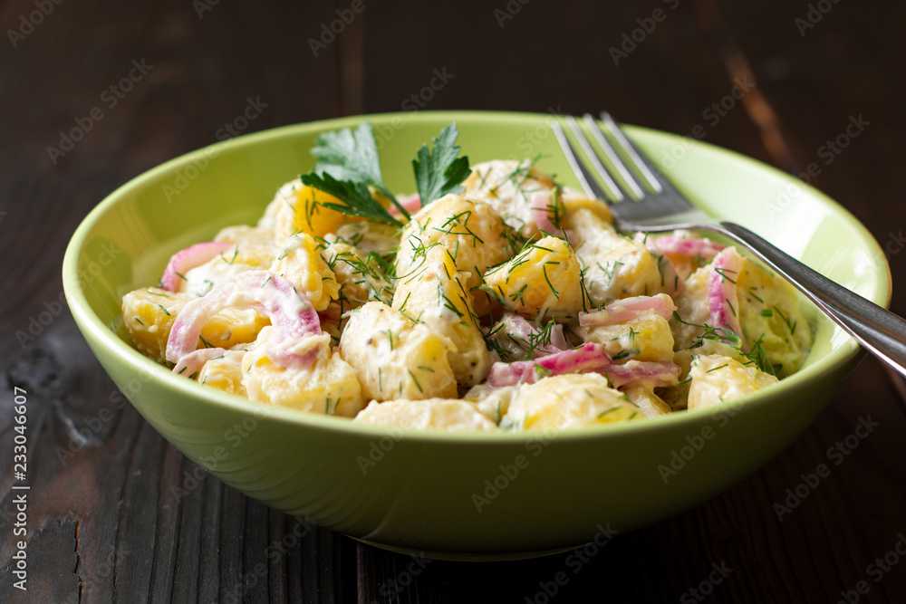 Potato salad with red onion and greens in bowl on dark wooden table. Selective focus.