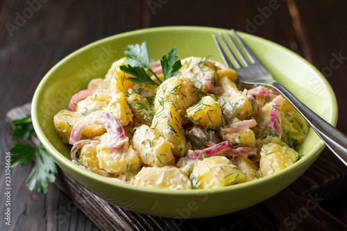 Potato salad with red onion and greens in bowl on dark wooden table. Selective focus.