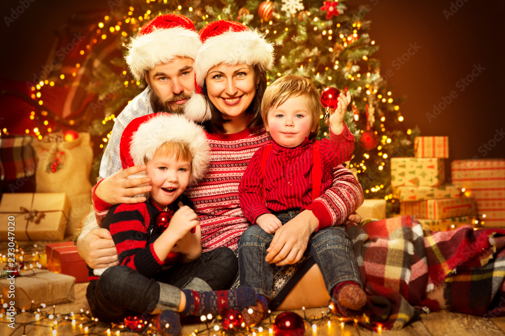 Christmas Family front of Xmas Tree, Happy Father Mother Child and Baby in Sweaters and Red Hat Christmas Family front of Xmas Tree, Happy Father Mother Child and Baby in Sweaters and Red Hat