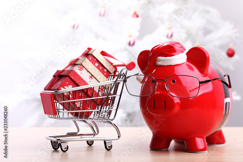 Valokuva Christmas piggy bank next to a shopping cart full of gift boxes