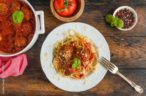 Pasta and meatballs with tomato sauce, white casserole and plate on wooden rustic table, top view