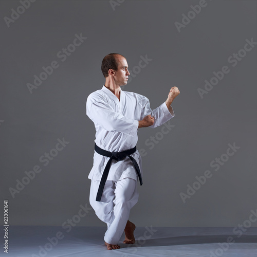 On a gray background, an active adult athlete trains formal karate exercises.
