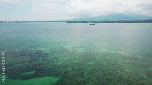 High angle view of beautiful green clear sea with corals beneath and distant ship, island and hill over horizon