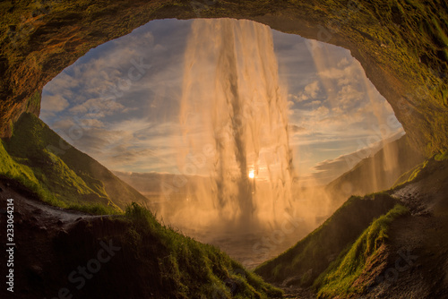 The waterfall Seljalandsfoss in the last golden light. One of the most famous waterfalls in Iceland. Shooted behind the waterfall at sunset. The sun's rays shine through the waterfall. © Petr Šimon